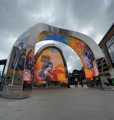 Large sculptural digital arch displaying colourful media in an outdoor public plaza