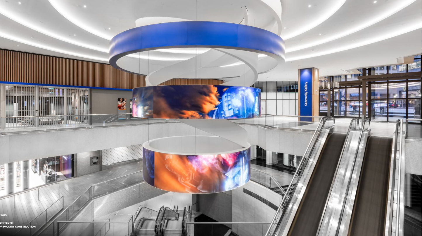Suspended circular LED ribbons carrying digital art through a multi-level retail atrium